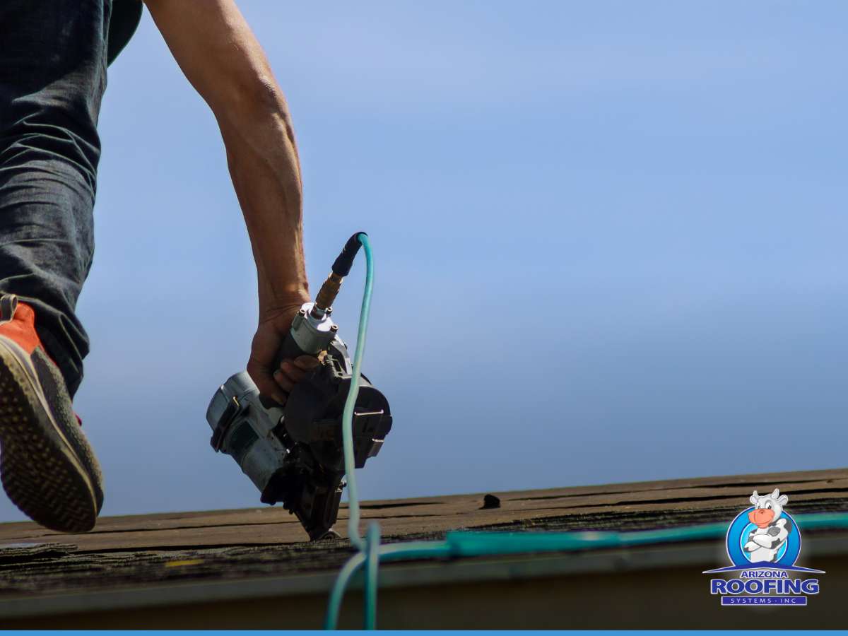 Roofing contractor performing roof replacement with pneumatic nail gun on a clear day